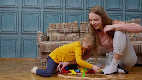 Mother with Little Daughter Child Girl Riding Toy Train on Wooden Railway Blocks Board Game at Home