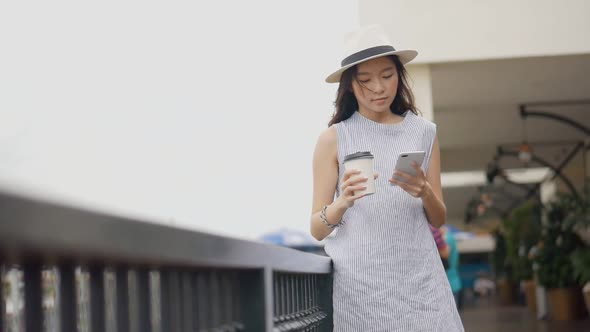 Young Asian woman using smartphone hand holding a coffee cup.