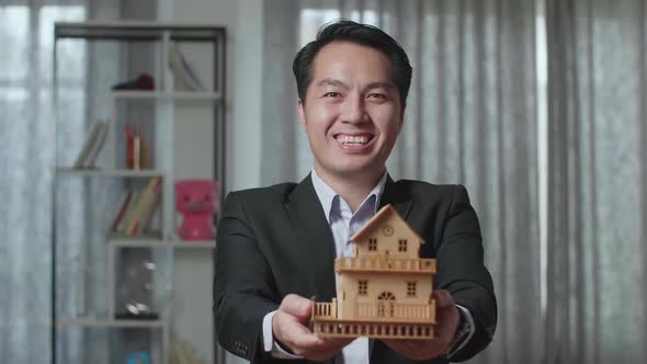 Close Up Of Asian Real Estate Agent Smiling And Showing House Model To Camera In The House For Sale