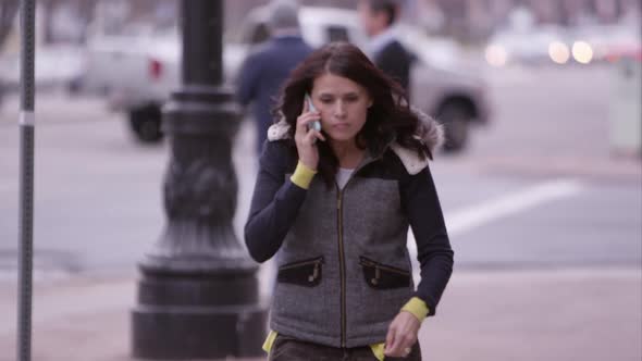 Close view of woman walking down the sidewalk answering call on cell phone.
