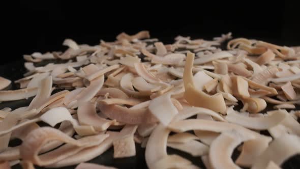 Coconut chips are falling down to the table, close-up, black background