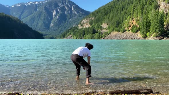 Man throwing a stone into crystal clear water. Snow Lake, Washington. In the background a snowy moun