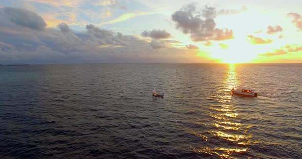 Aerial drone view of a man and woman sailing on a boat to a tropical island at sunset