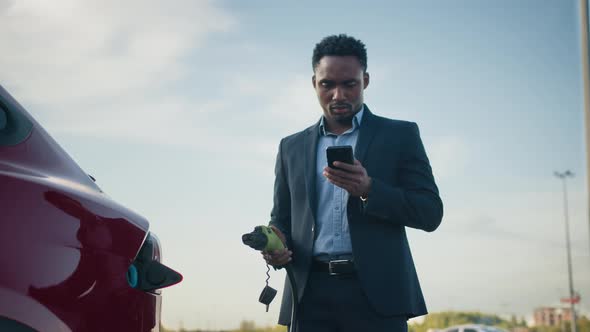 Close Up of African Businessman Unplugging Charging Cable From Electric Car