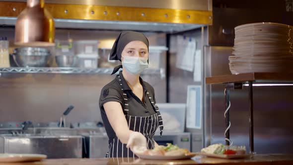 Confident Young Woman in Coronavirus Face Mask Putting Plate with Salad on Counter in Slow Motion