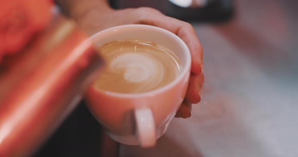 Barista pouring milk into a coffe cup, creating flower pattern