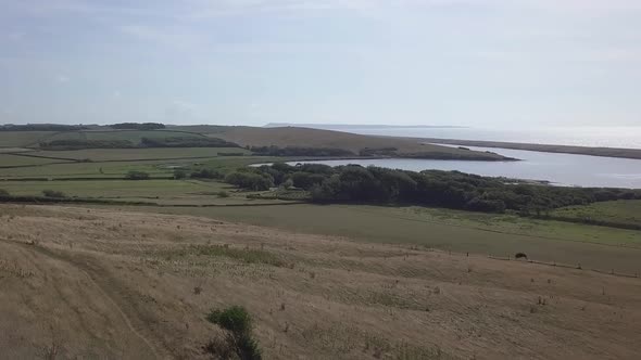 Low forward tracking aerial down a hill towards the fleet lagoon at the west end of Chesil Beach. Ab