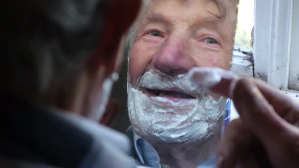 Old Grayhaired Older Grandfather Applying Foam to Face for Shaving and Looking in the Mirror