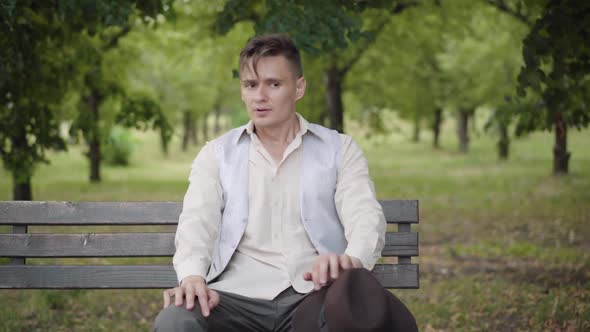 Unhappy Nervous Elegant Man Sitting on Bench in Summer Park and Looking Around. Portrait of Young