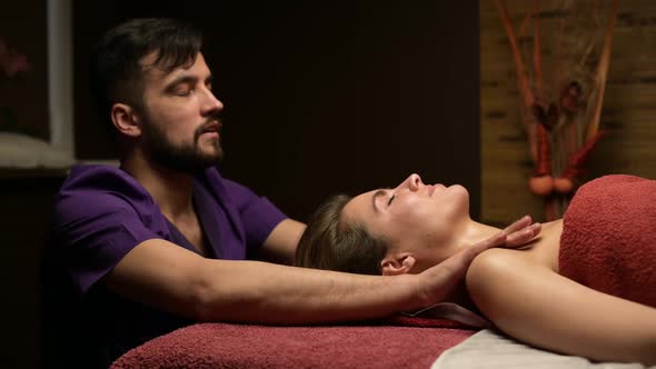 A man masseur kneads the shoulders of a young woman on a massage table
