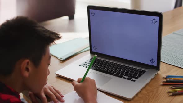 Asian boy at home, writing during online school lesson using laptop, with copy space on screen