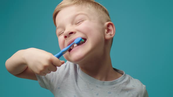 Preschool Boy Enjoys Brushing Teeth Standing Alone with Closed Eyes on Blue Background
