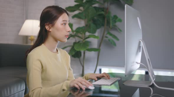 Young Asian Businesswoman Working From Home and Typing Using Desktop Computer in Living Room