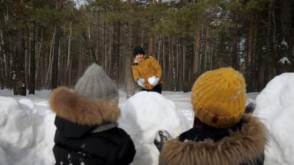 Man is Playing Snowballs with His Family Wife and Little Son Hiding Before Snow Wall