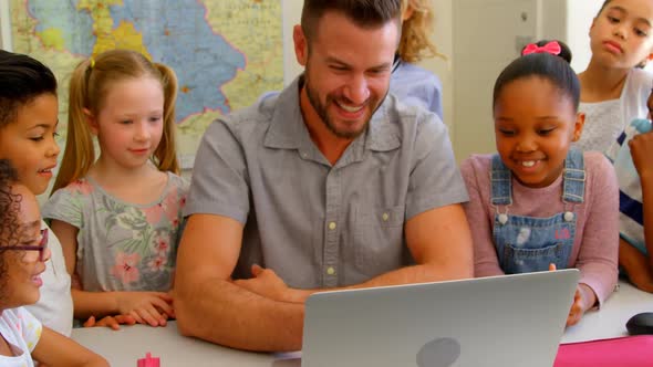 Caucasian male teacher teaching school kids on laptop in classroom at school 4k