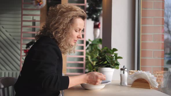 Young Curly Woman Eating Cream Soup In Cafe