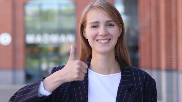 Thumbs Up By Business Woman at Work Looking at Camera