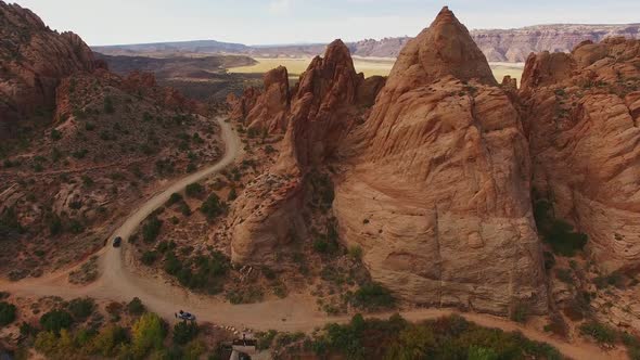 Ascending footage over red rock with vehicle on road in Moab