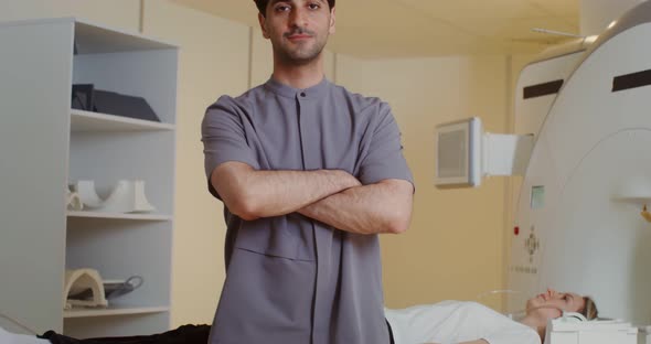 A Doctor Looks Into the Camera Standing in Front of an MRI Machine