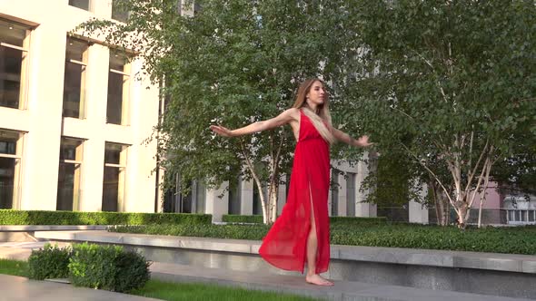 Beautiful Young Girl Dancing on Green Grass Against the Background of a Modern City. She Is Wearing