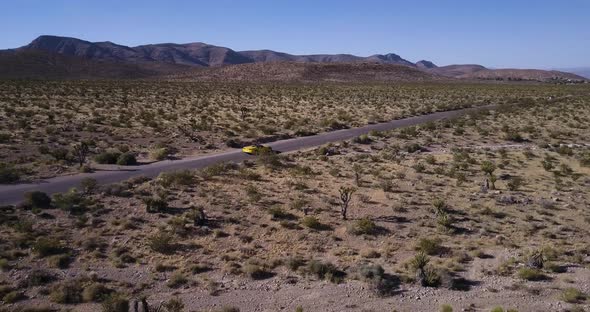 Aerial view of yellow sport car driving on asphalt road in the middle of dusty dry desert land.