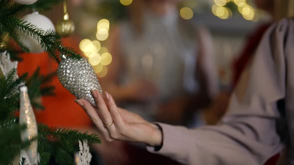 Closeup of a Woman's Hand and a Silver Cone Hanging on a Christmas Tree