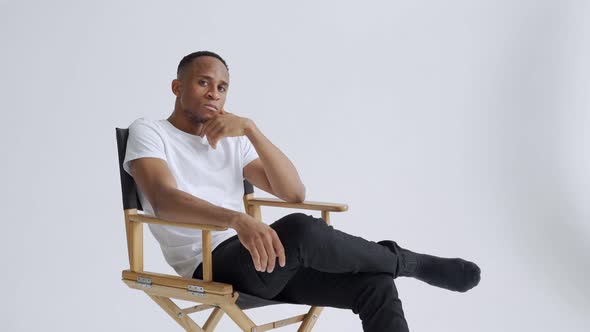 Dreamy Athletic Relaxed Black Young Man Sitting on a Armchair Against White Wall Backgroun