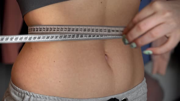 Girl With a Beautiful Figure Measures Her Waist with a Measuring Tape