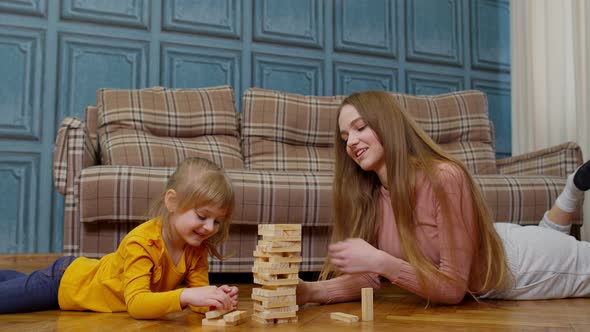 Happy Young Mother Woman Teaching Small Child Daughter Playing Wooden Blocks Board Game at Home