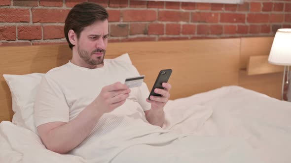 Casual Young Man with Unsuccessful Online Payment on Smartphone in Bed