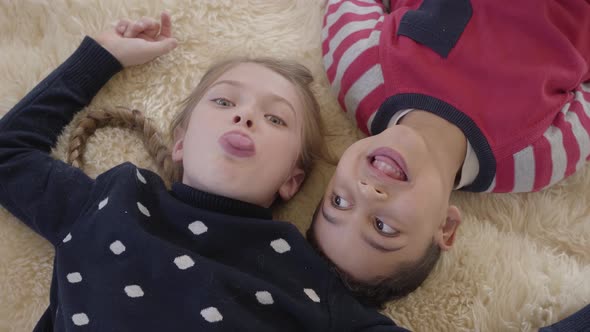 Portrait African American Boy and Blond Caucasian Girl Lying on the Floor on the Beige Fluffy Carpet