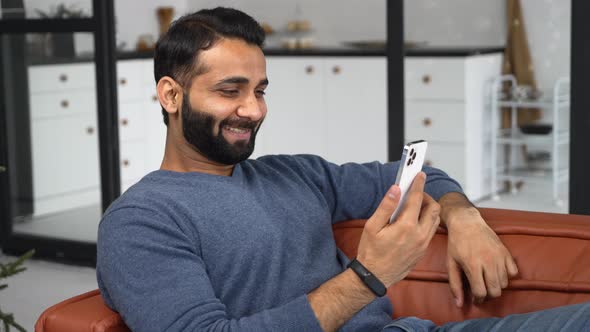 Happy Young Bearded Indian Eastern Man Holding Cellphone and Making Video Call