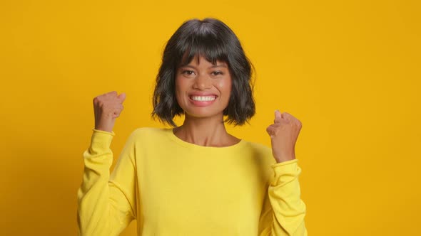 Happy Woman Makes Fist Pump with Triumph Celebrates Success on Yellow Background