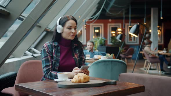 Girl in Headphones Enjoying Music and Using Smart Phone at Table in Cafe