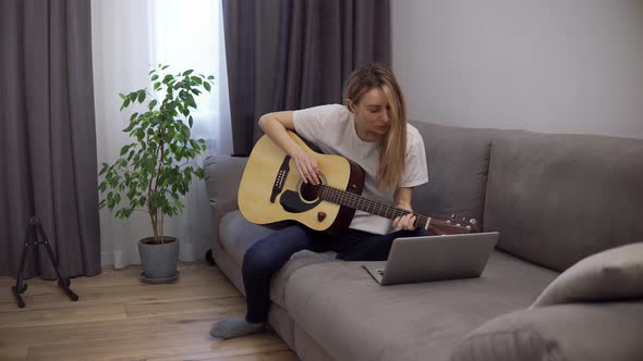 A Young Woman Plays the Guitar Through a Video Call on a Laptop