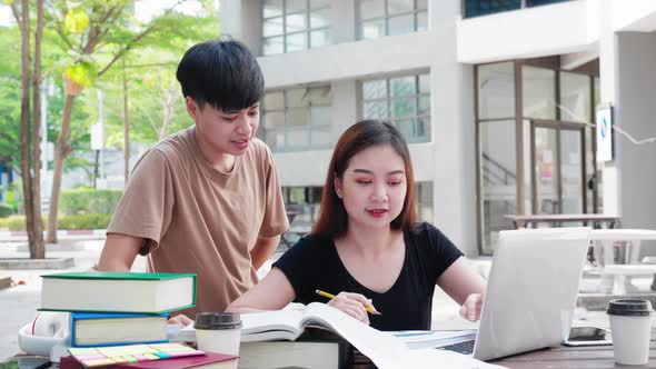 Two teenage Asian university students doing study research, arguing in library with books on desk