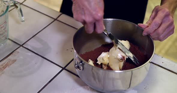 A chef in a kitchen putting vegan butter into a metal mixing bowl while baking a chocolate cake for