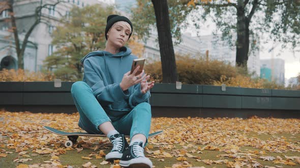 Young Caucasian Hipster Woman Using Phone To Make Selfie in the Park Covered in Autumn Leaves While