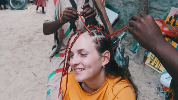 African Woman Weaving African Braids with Red Kanekalon Outdoor Zanzibar Africa