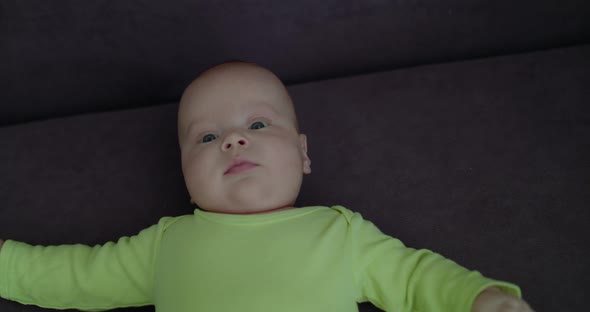 Funny Baby Boy Lying on Sofa with Open Arms and Looking Around