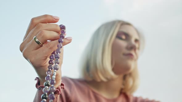 Hand of Young Believing Woman Prays in Nature and Uses Craft Rosary Beads To Count Prayer and alt