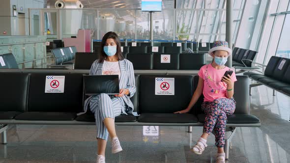 Woman and Teenage Girl, in Protective Masks, Use Mobile and Laptop, While Sitting in Empty Airport