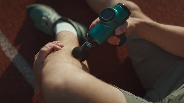 A Male Athlete Massages Muscles and Tendons with a Massage Percussion Device After a Workout at the