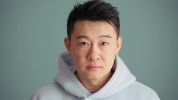 Handsome Asian man wearing hoodie opening his eyes at the camera