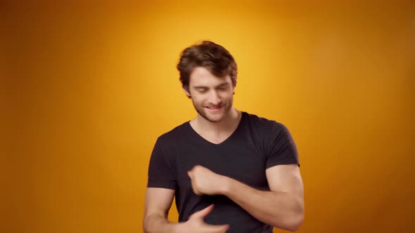 Happy Young Bearded Man Dancing with His Hands Against Yellow Background