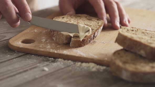 Man Spreads Philadelphia. Whole Slices Sourdough Bread On A Bamboo Board. Close Up Shot Of A Knife