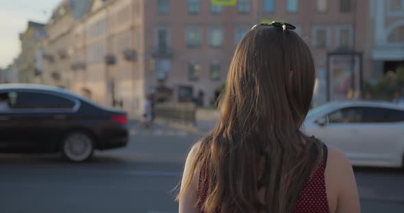 A Girl with Long Hair Stands in Front of the Road on Which Cars are Driving