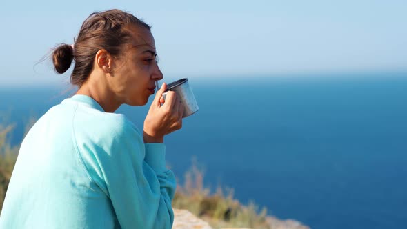 Outdoors Portrait Carefree Smiling Woman Sitting on Cliff Edge with Beautiful Sea View, Holding Mug