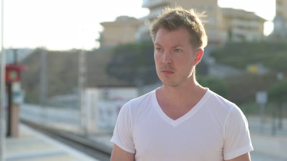 Young Handsome Tourist Man Smiling While Thinking At The Train Station