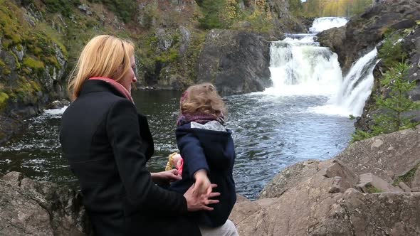 A Young Mother and Her Cute Daughter Looking at the Cascade of a Forest